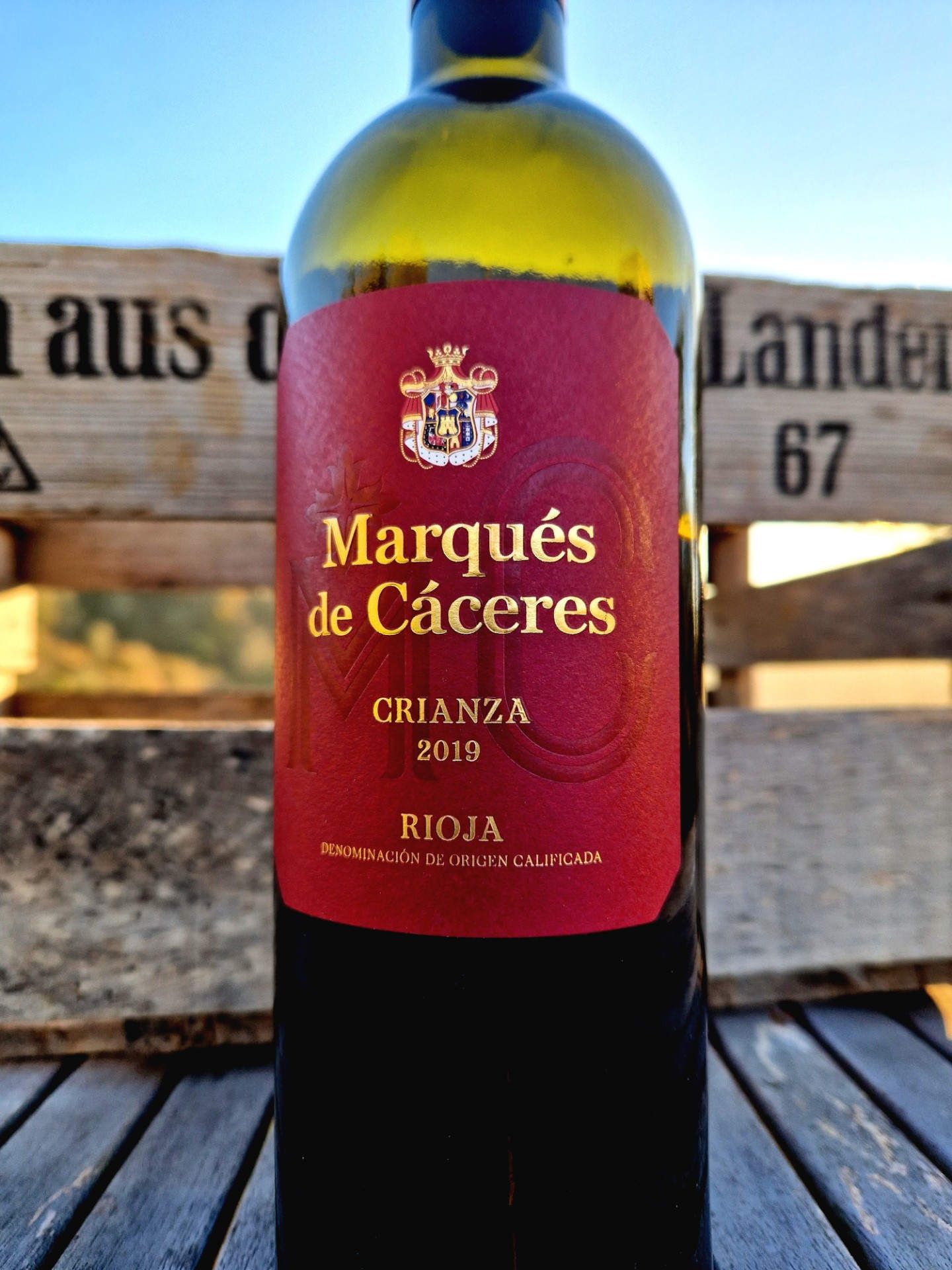 Eine Rotwein-Crianza von Marqués de Cáceres auf einem Tisch vor einer Holzkiste