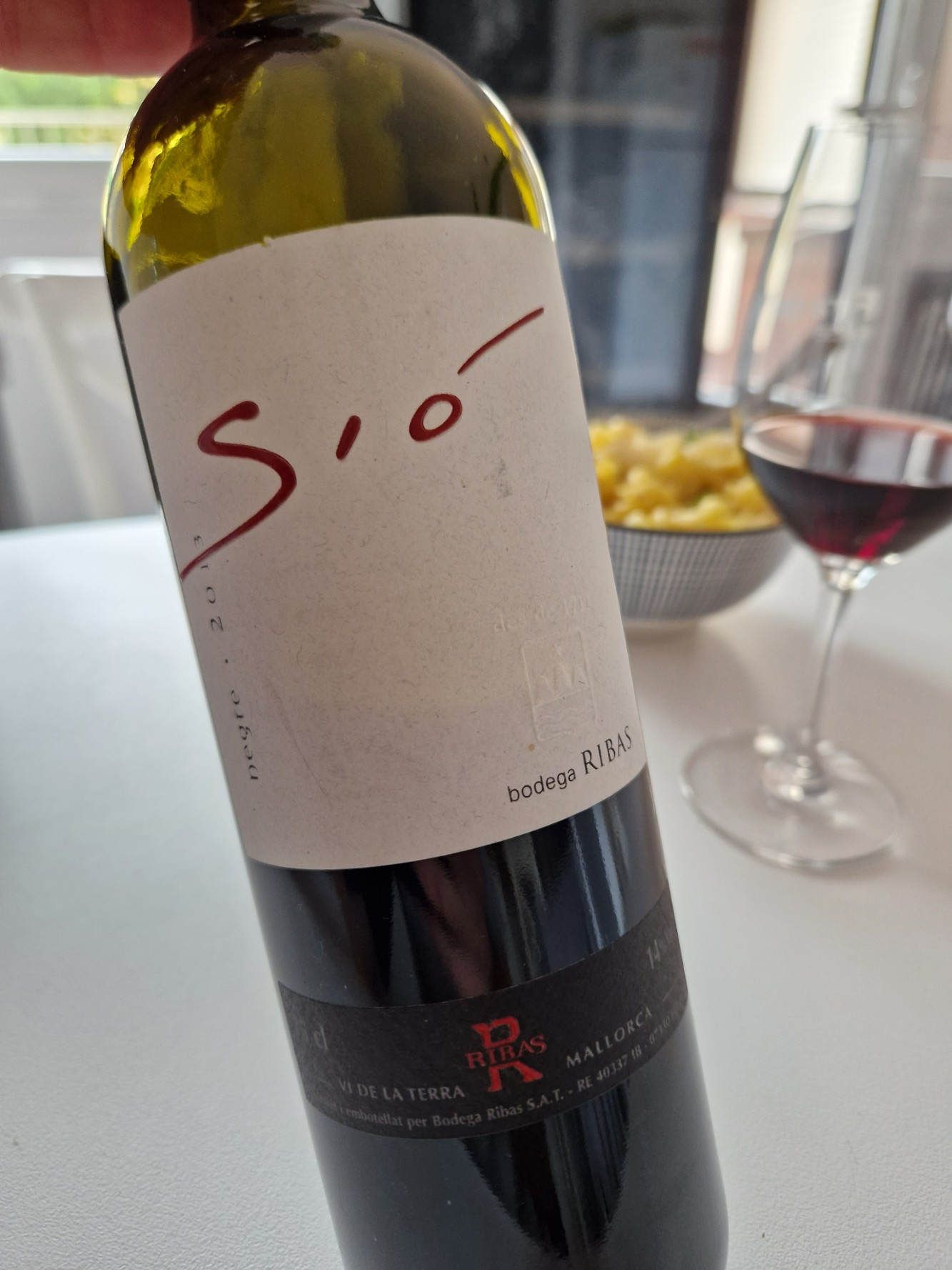 Eine Flasche Rotwein und im Hintergrund ein halbvolles Glas auf dem Tisch