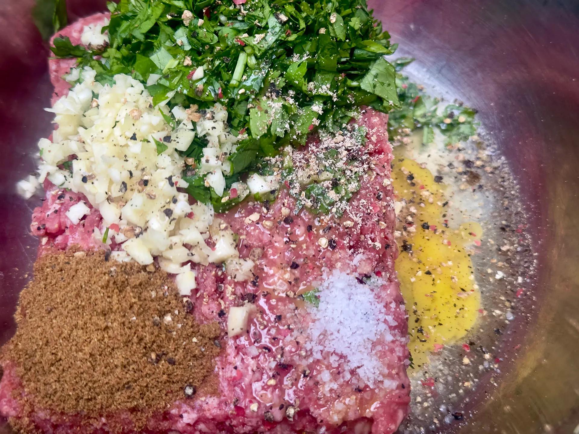 Zubereitungsschritt für ein Albóndigas Rezept: Frisches Hackfleisch in einer Schüssel, verfeinert mit gehacktem Knoblauch, Kräutern, Ei und Gewürzen.