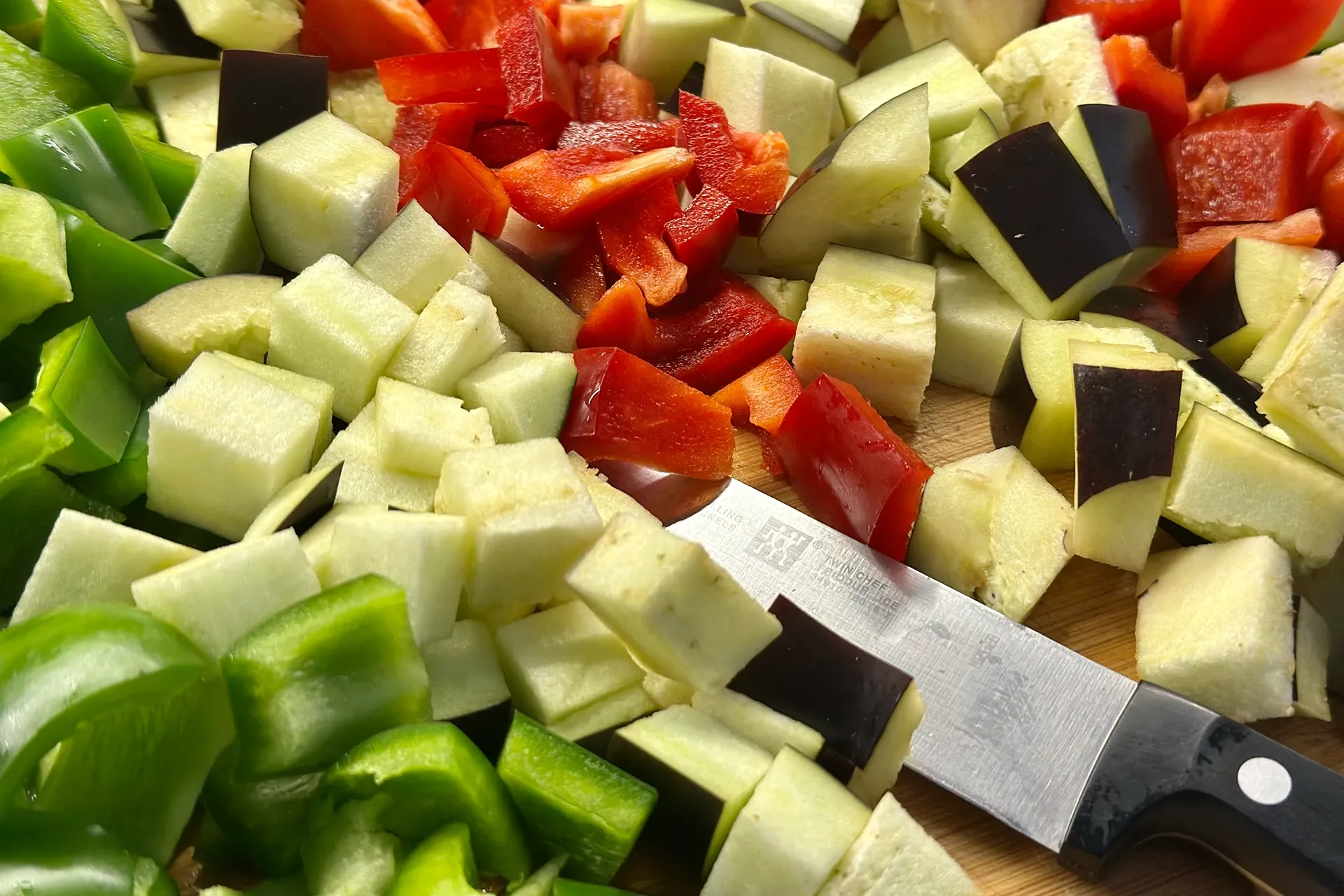 Gewürfelte grüne und rote Paprika und Aubergine liegen neben einem Schneidemesser