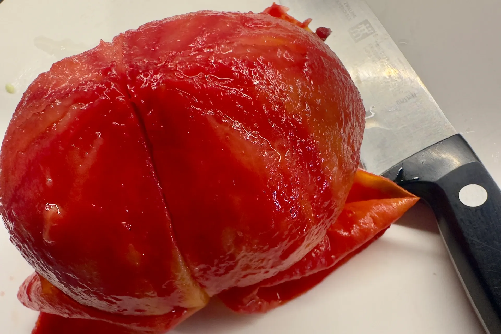 Eine geschälte Tomate liegt neben einem Schneidemesser