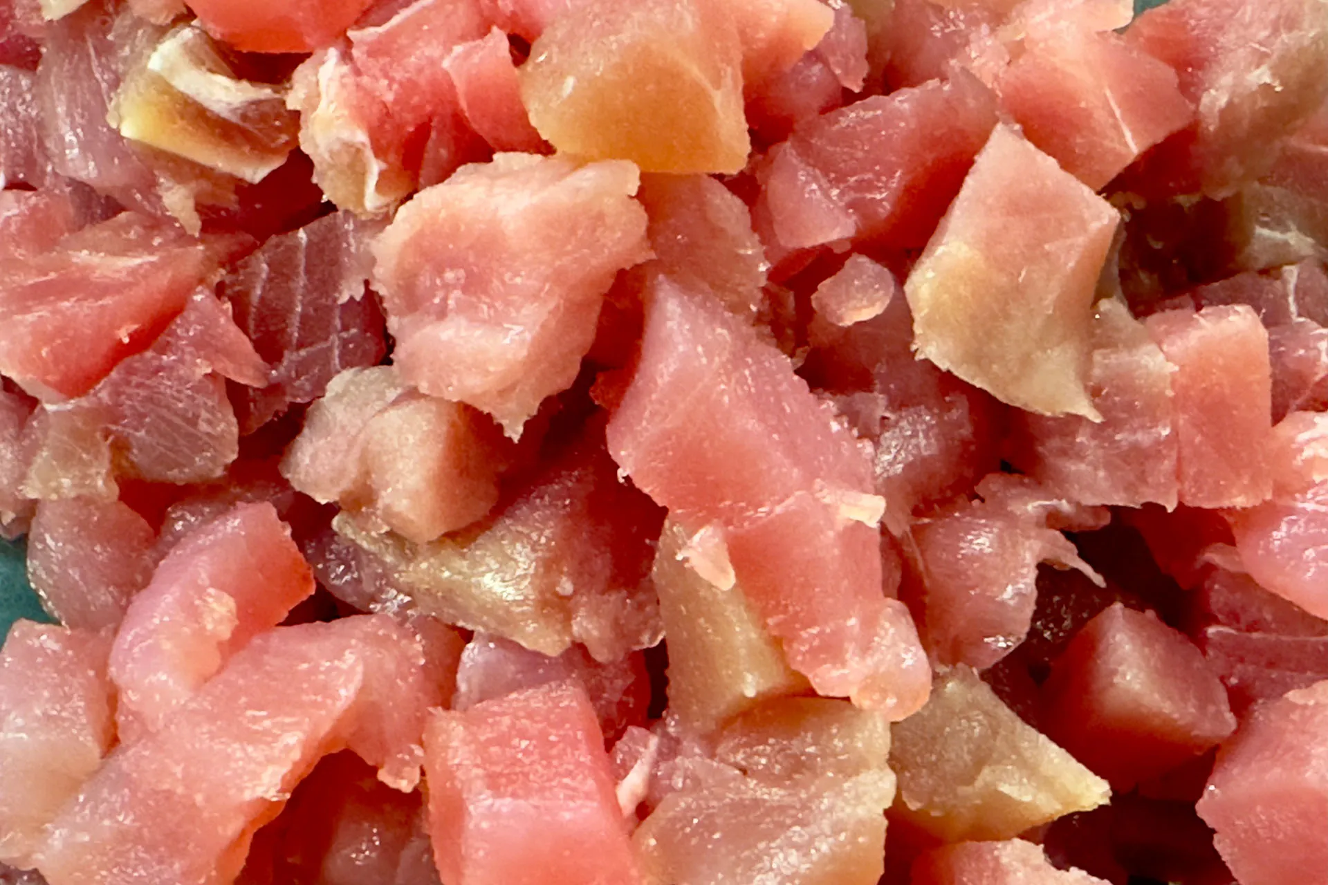 Frischer roher Thunfisch in gleichmäßige kleine Würfel geschnitten auf grünem Schneidebrett