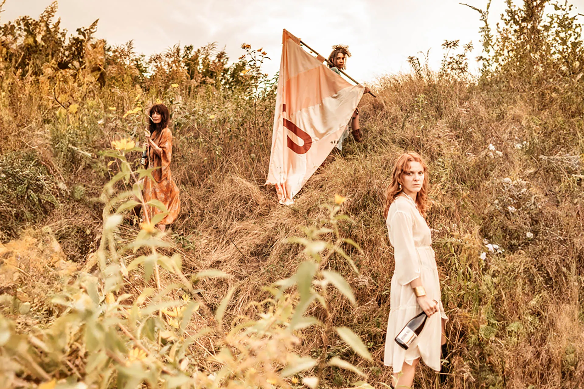 drei junge Frauen mit Fahne in einer Landschaft mit Weinflasche