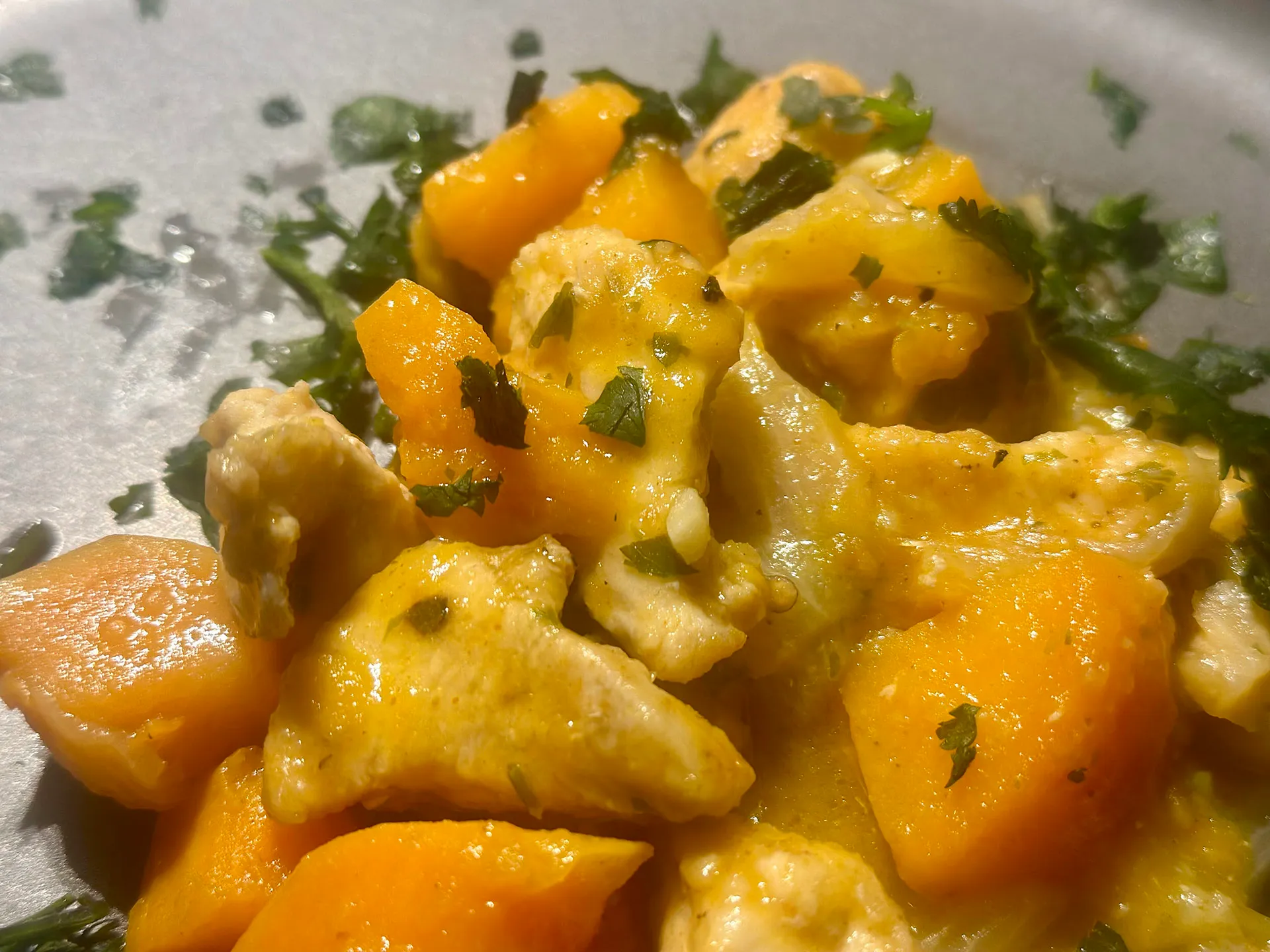 Teller mit einem Hühnchen, Süsskartoffeln und mit Petersilie und Koriander angerichtet