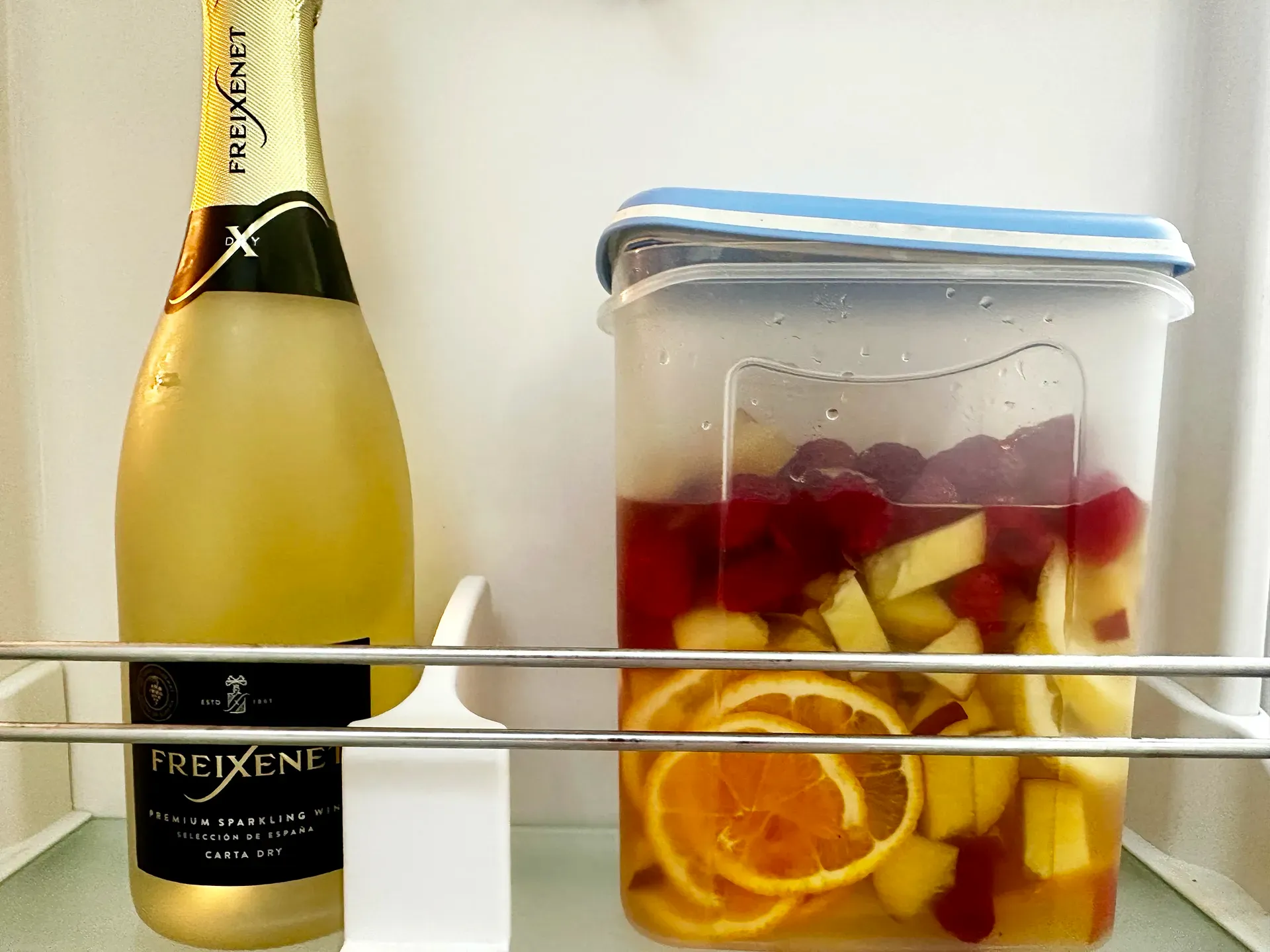 Flasche Cava und ein Plastikbehälter mit Früchten