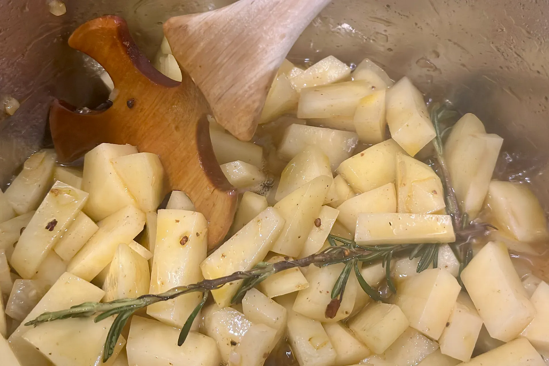 Kartoffeln kleingeschnitten in einem Topf und werden angebraten mit einem Rührlöffel