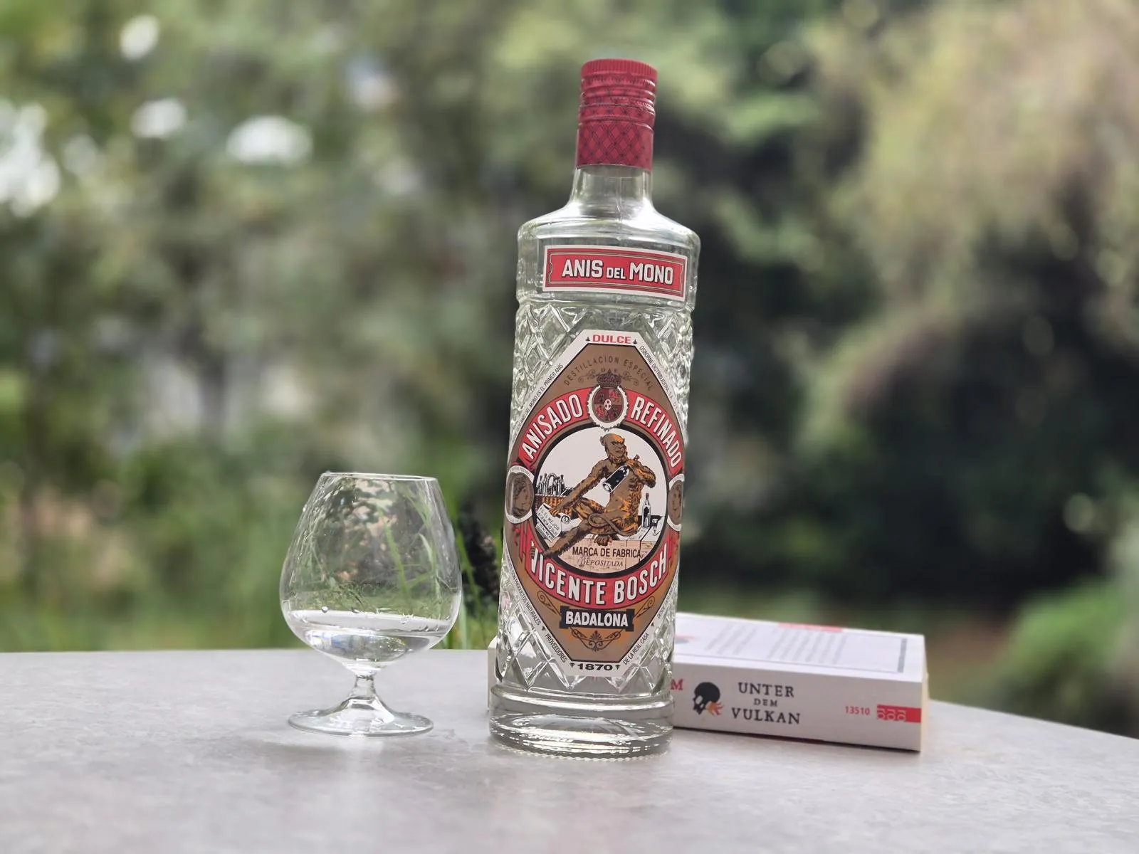 EIne Flasche Anisschnaps mit einem Glas und einem Buch auf einem Tisch