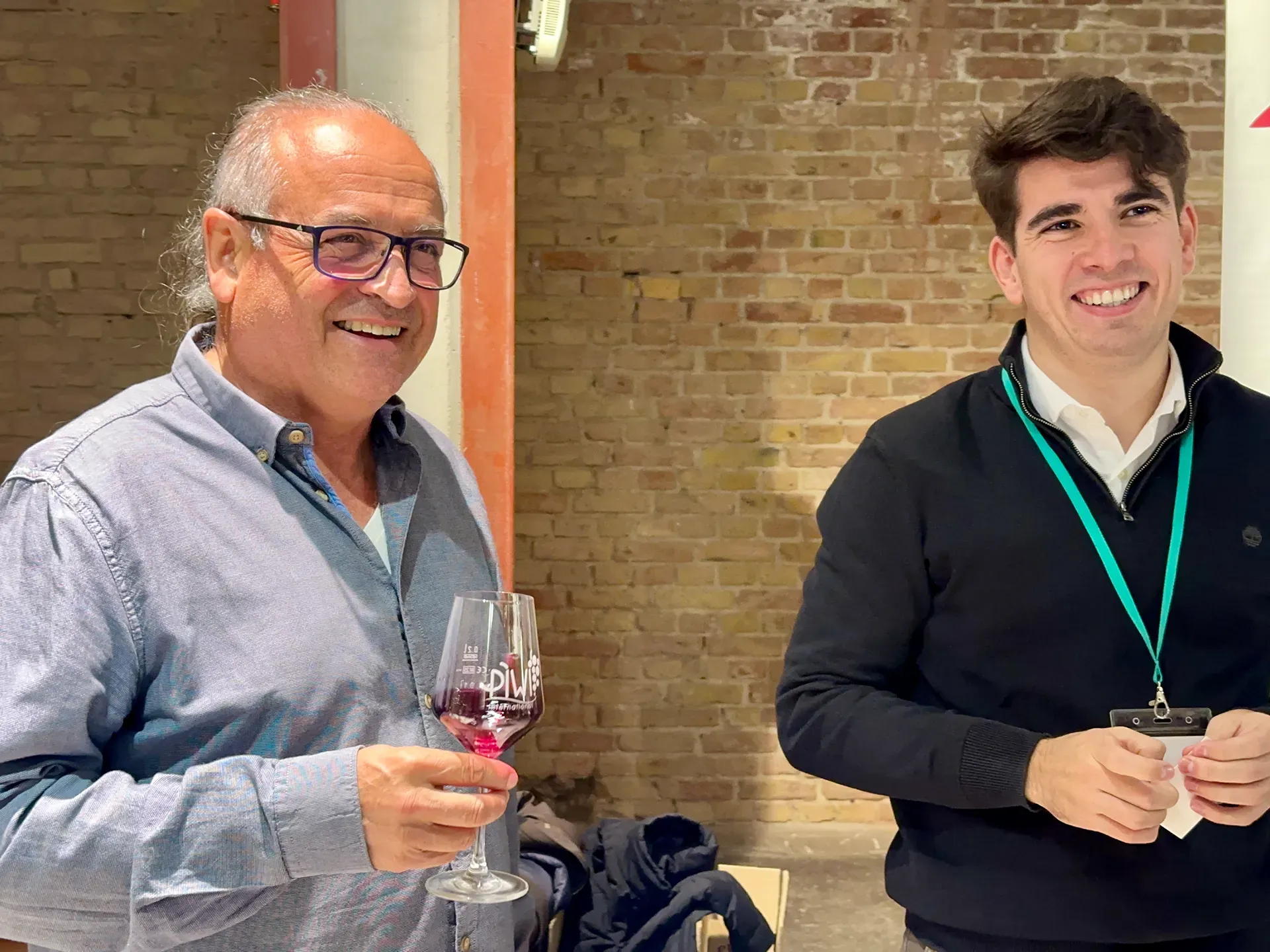 Zwei Männer stehen vor einer Ziegelmauer und halten zwei Weingläser in der Hand