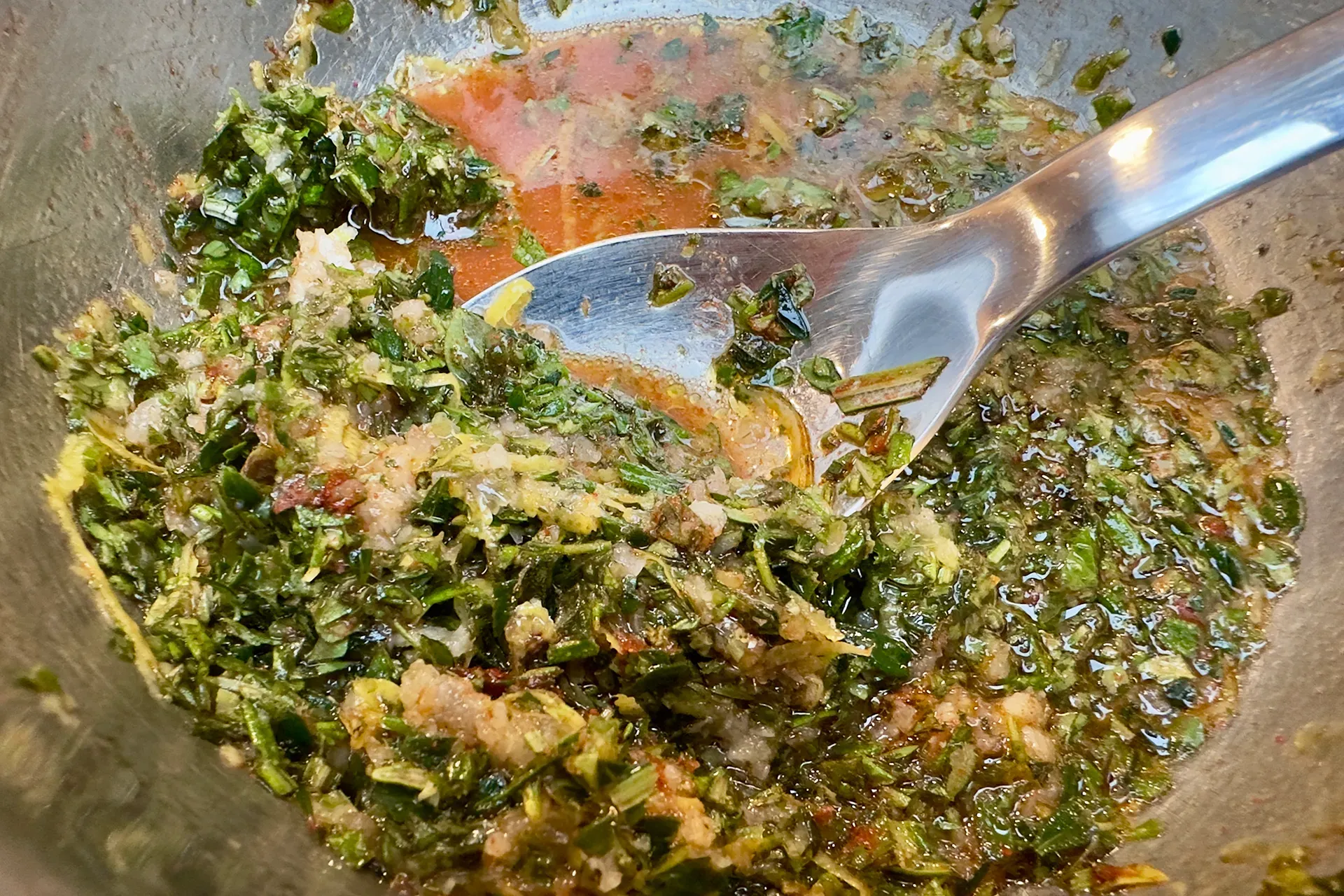 Eine Edelstahlschüssel mit einem Löffel und vielen Kräutern für eine Sauce