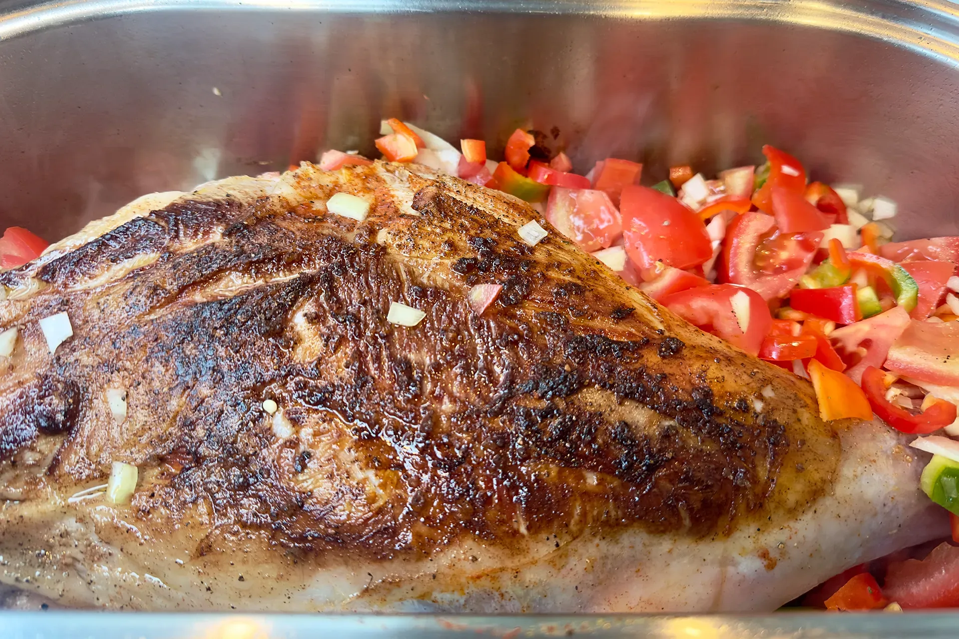 Ein Stück Fleisch in einem Bräter mit Gemüse dabei