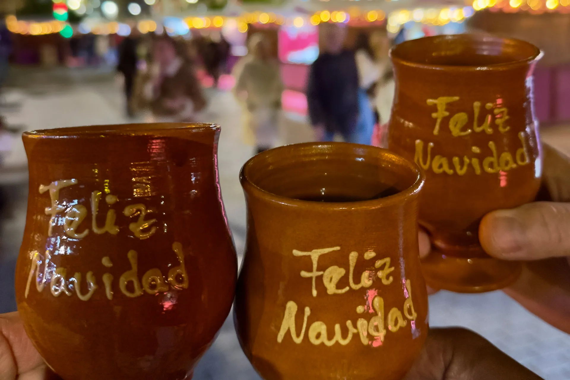 drei handgefertigte Becher mit der Aufschrift Feliz Navidad - sie werden in Händen gehalten