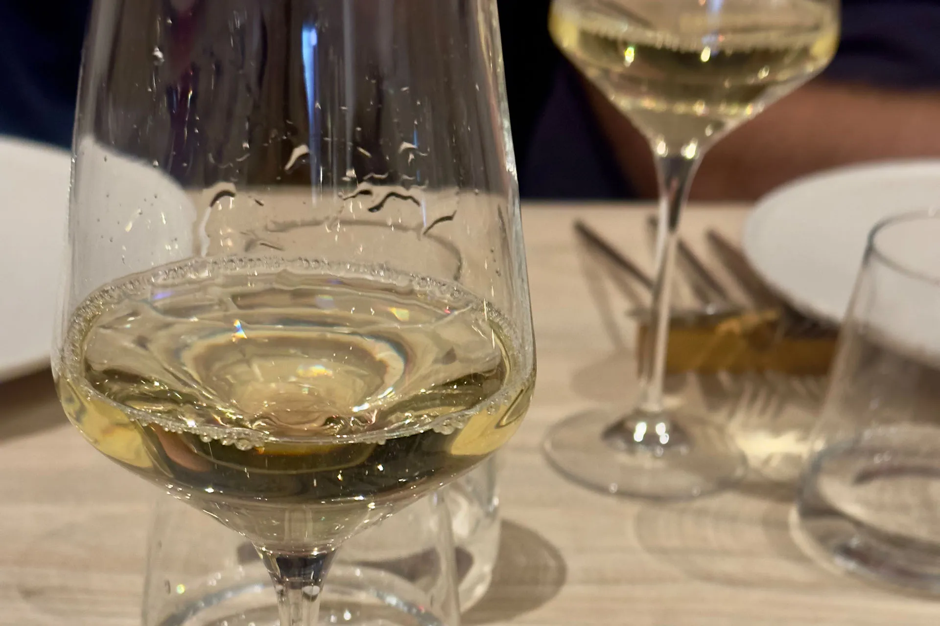 Zwei Weingläser mit Weißwein auf einem gedeckten Tisch, im Vordergrund ein fast leeres Glas