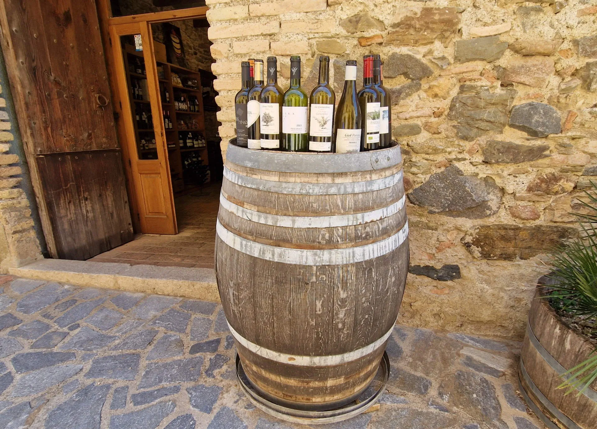 ein Weinfass vor einer Hauswand, auf dessen Deckel leere Weinflaschen stehen.