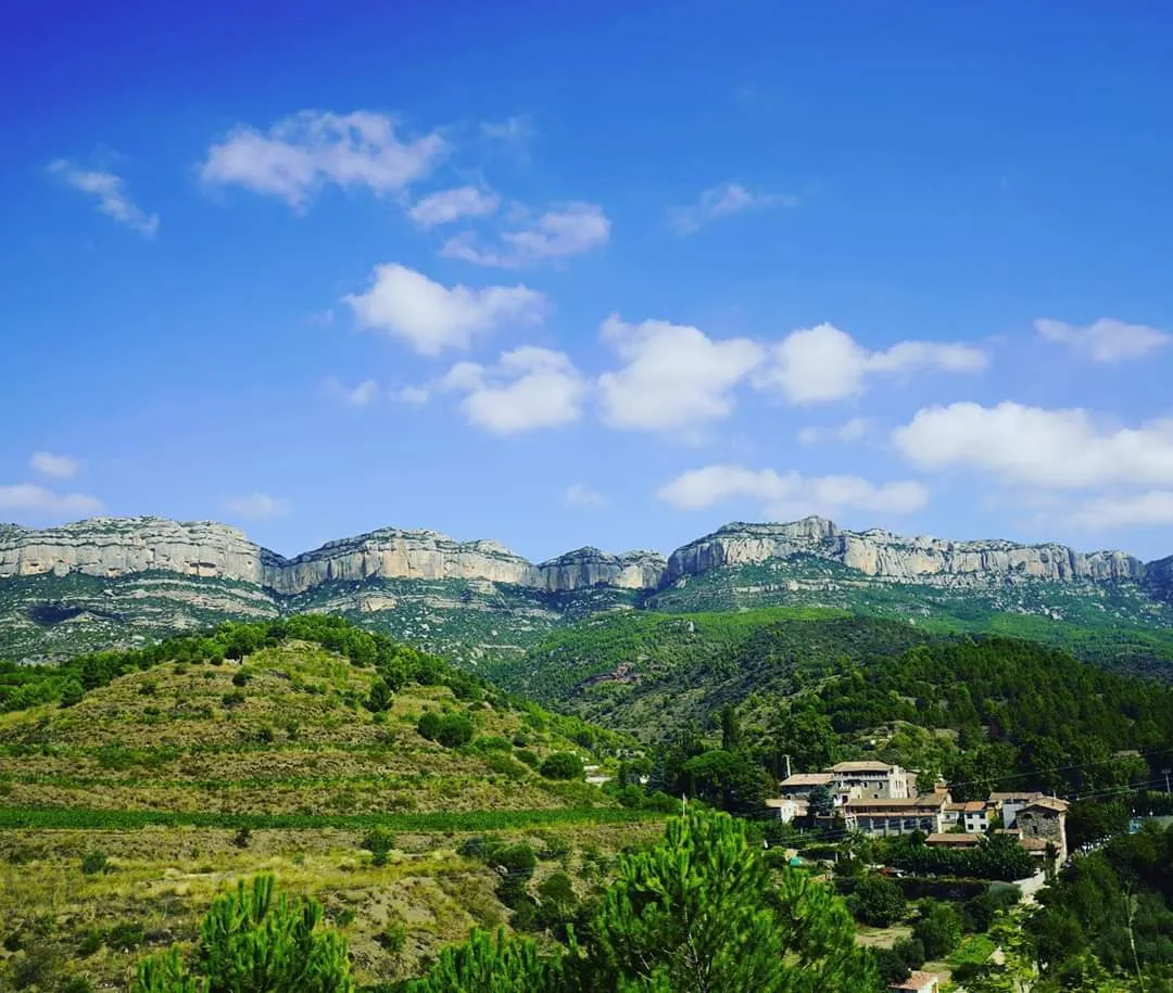 Blick auf ein kleines Dorf, dahinter hochaufragende Felswände