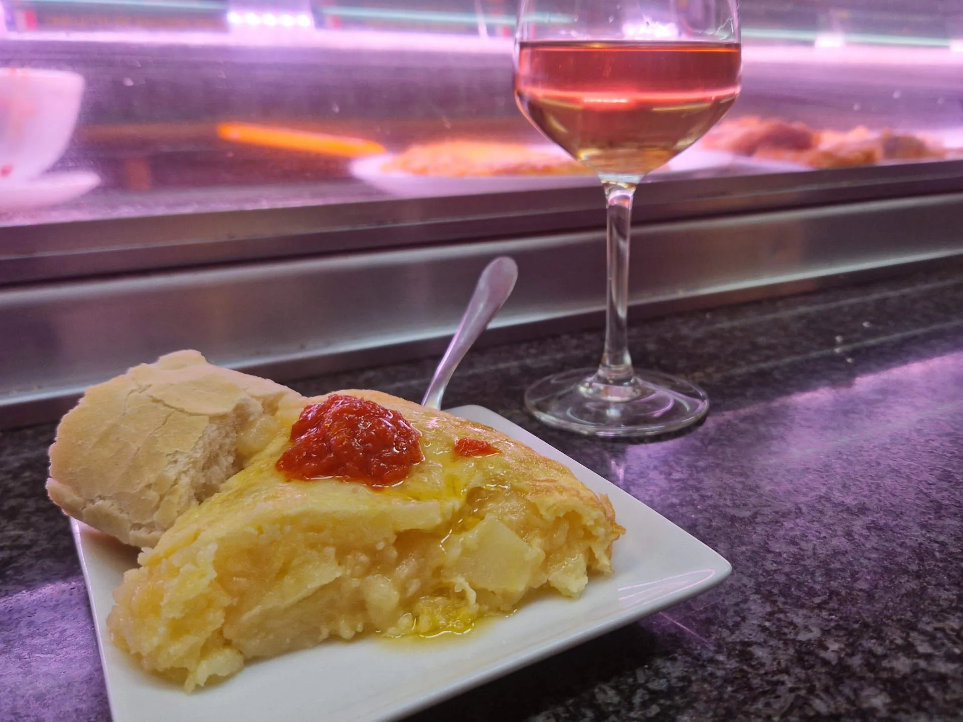 Ein Teller mit einem Stück Tortilla und einem Glas Wein im Hintergrund