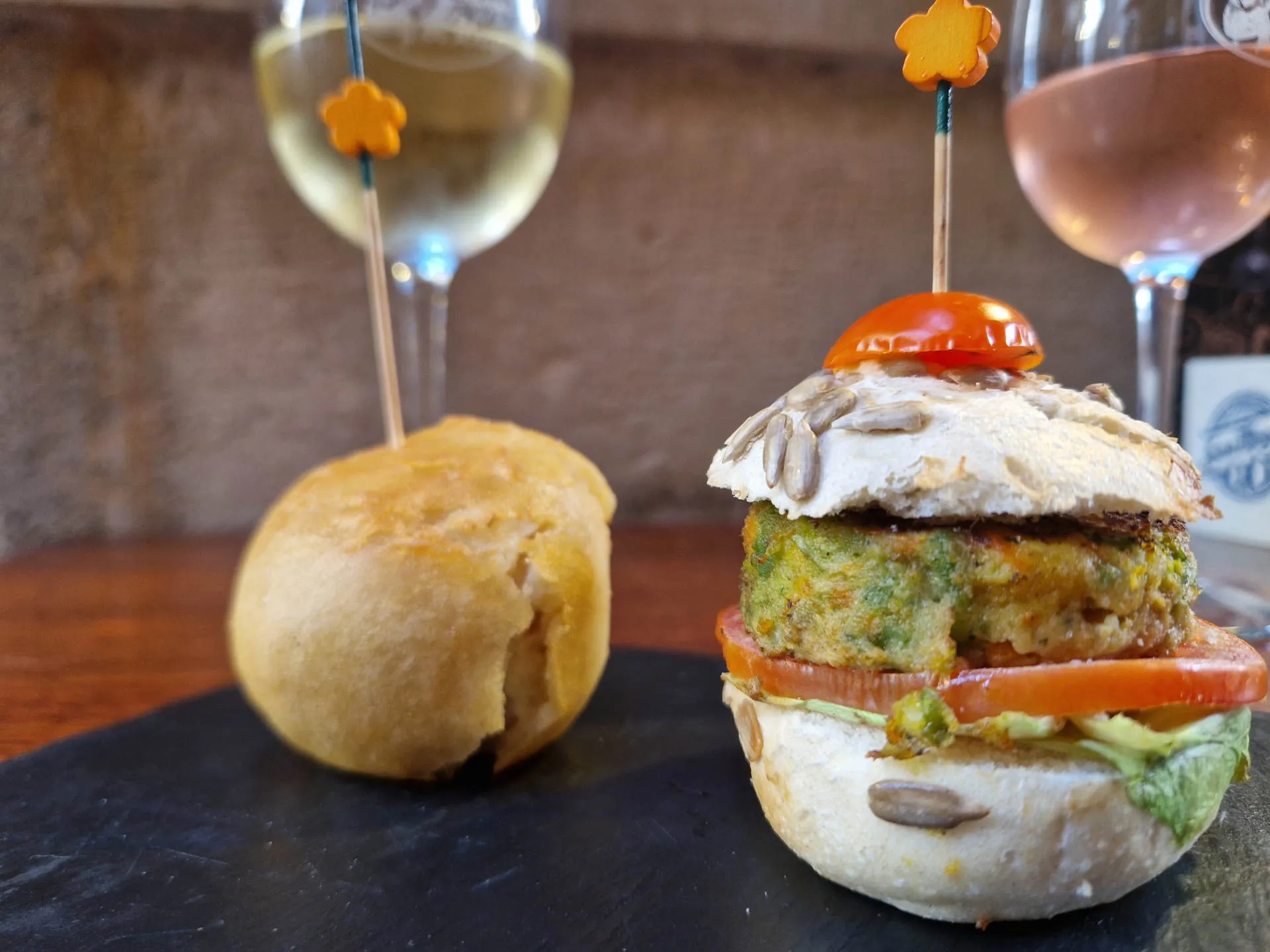 Ein Mini-Burger auf einem Spieß und ein Glas Wein im Hintergrund