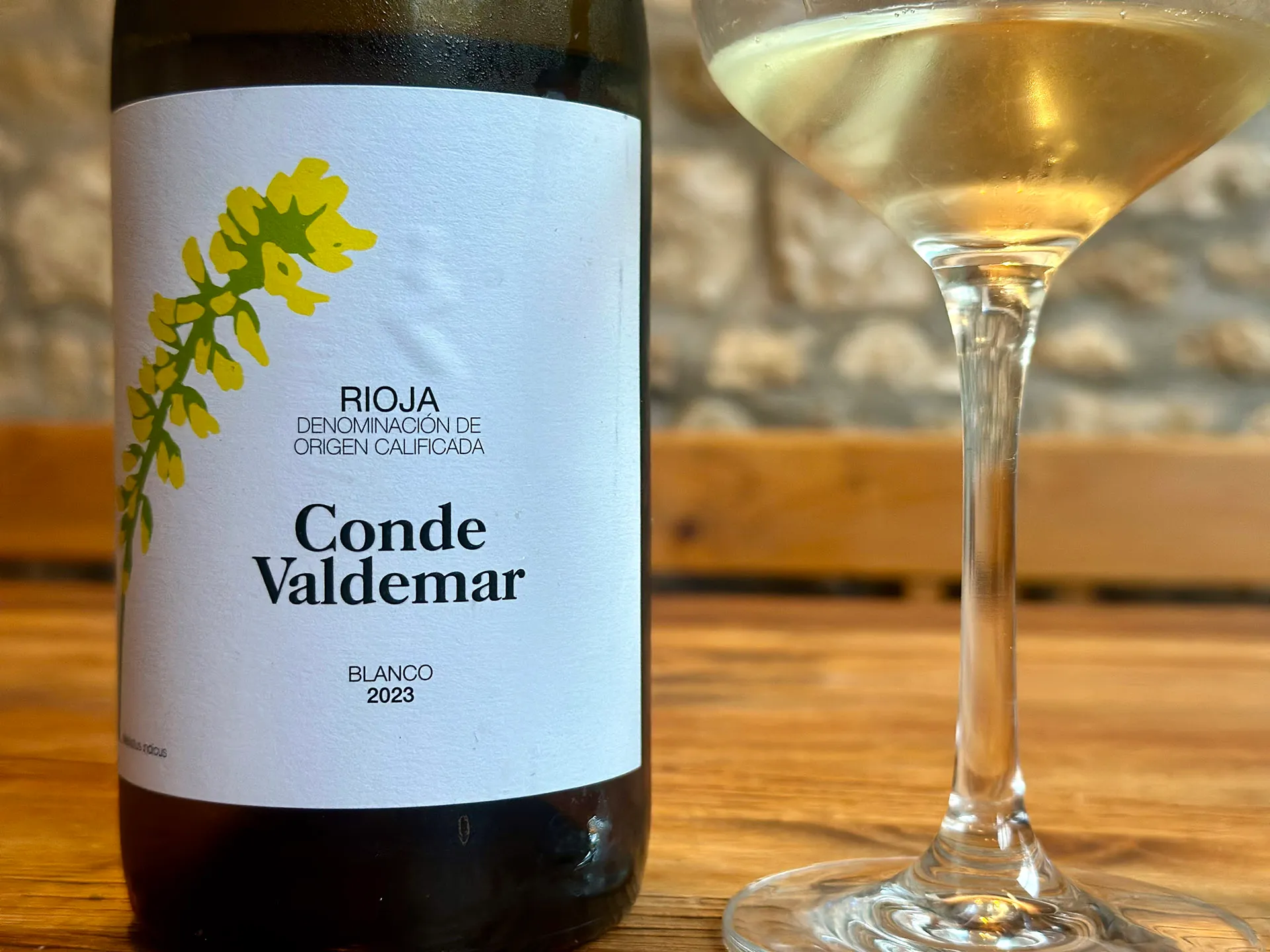 Weinflasche mit einem gelb grünen Etikett und Glas mit Weißwein